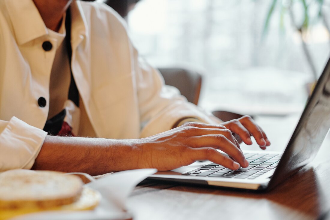 Hands typing on a laptop at a wooden table, breakfast beside it