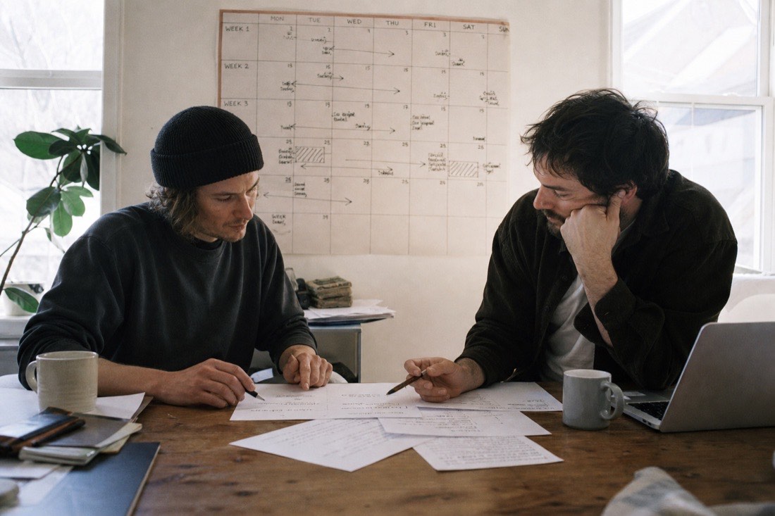 Two musicians mapping a release on paper with a wall calendar behind them